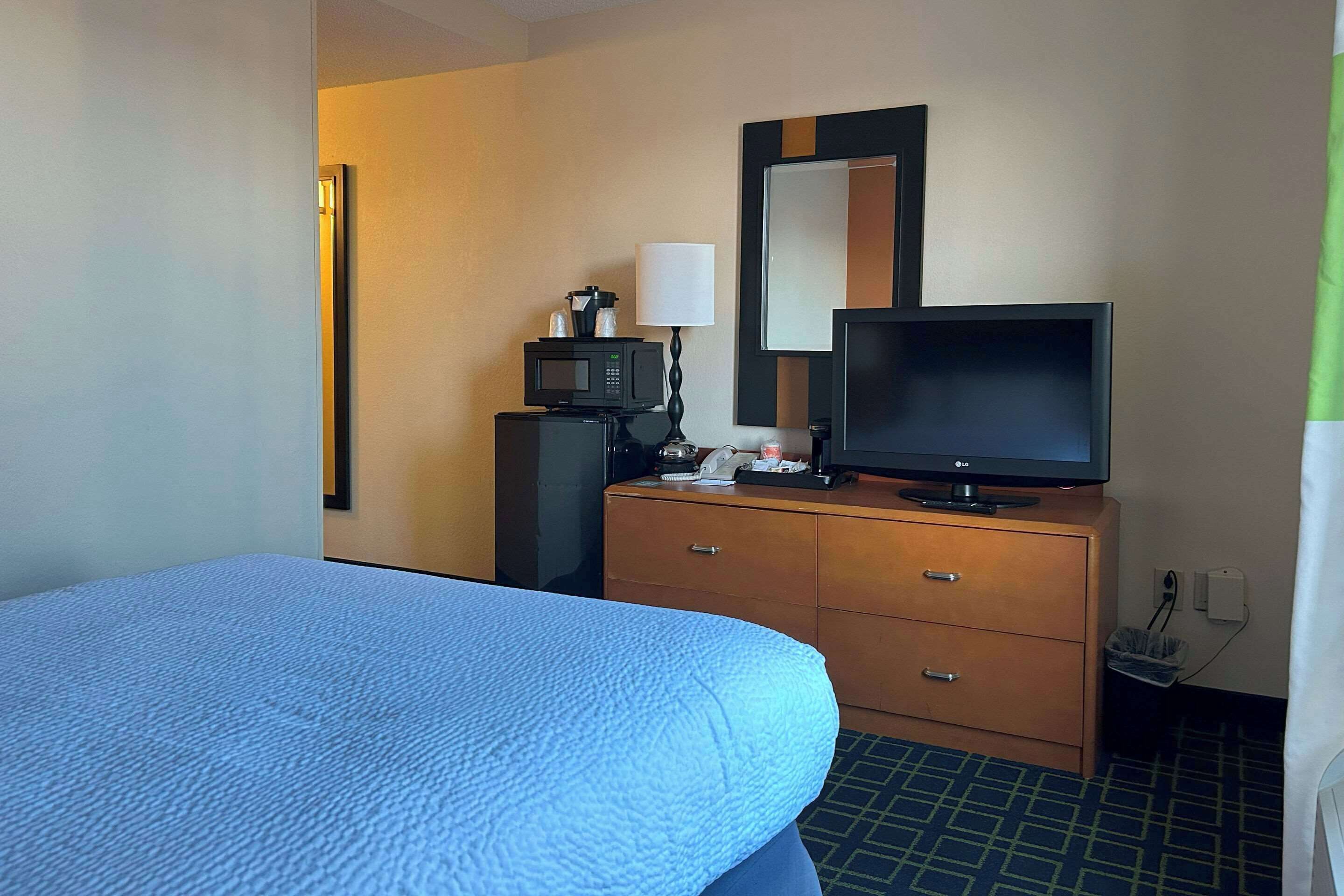 Une chambre d’hôtel équipée d’un lit, d’une télévision, d’un four à micro-ondes, d’une lampe et d’une commode.