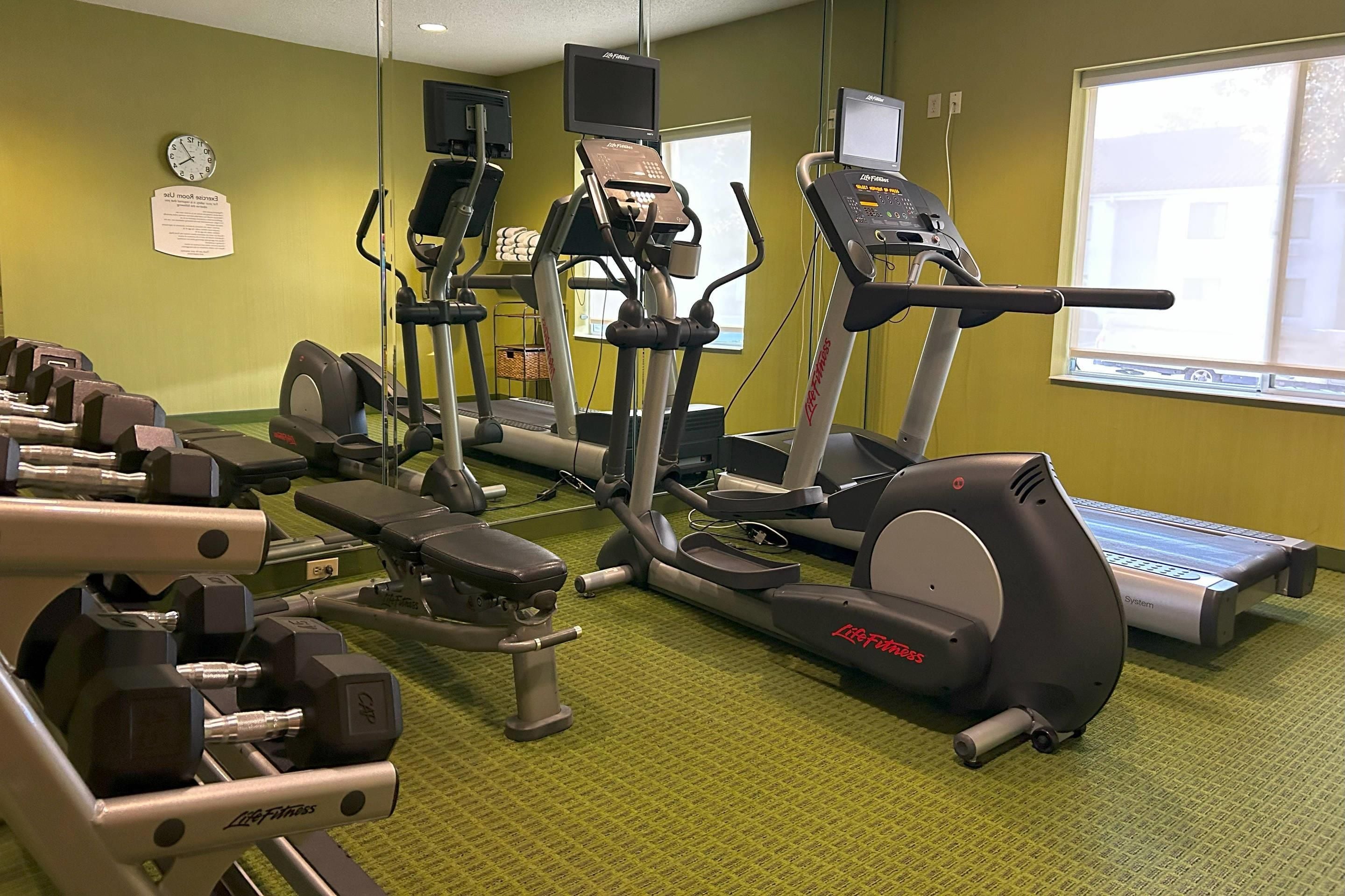 Un gimnasio con diversos equipos de ejercicio, incluyendo cintas de correr, elípticas y bancos de pesas.