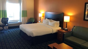Ein Hotelzimmer mit einem Bett, zwei Nachttischlampen, einem Schreibtisch, einem Sessel, einer Couch und einem Fenster mit Vorhängen.
