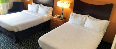 A hotel room with two beds, a nightstand with a lamp, a telephone, and a chair.