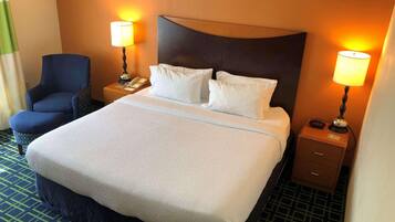 A hotel room with a large bed, two bedside lamps, a chair, a nightstand, and a wall-mounted clock.