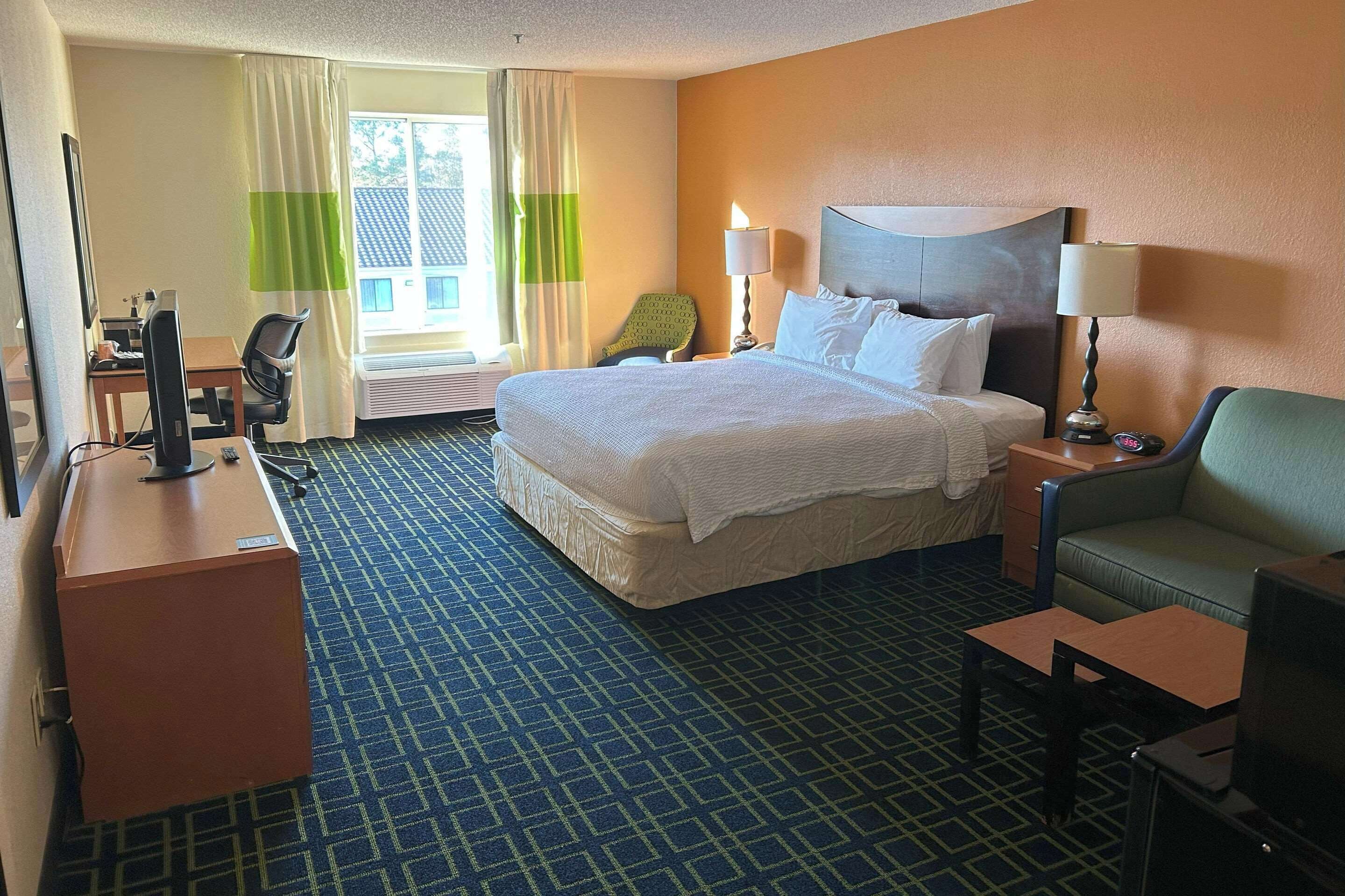 A hotel room with a large bed, a desk with a computer, a chair, a TV, and a sofa.