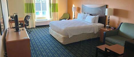 A hotel room with a large bed, a desk with a computer, a chair, a TV, and a sofa.