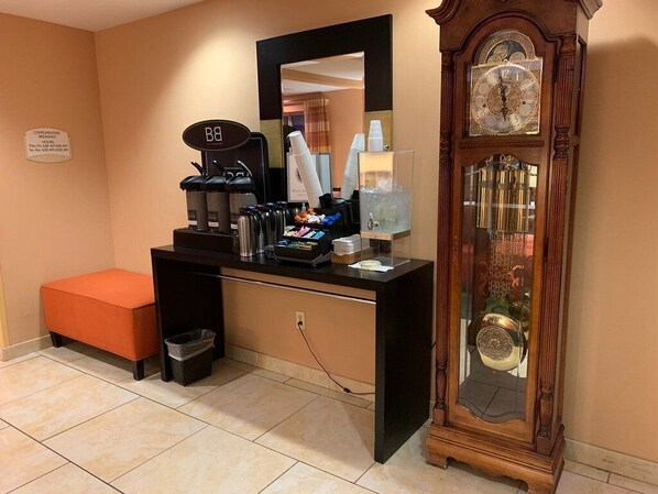 A hotel room with a coffee station, a large clock, and a trash bin.