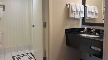 A bathroom with a shower, toilet, sink, and a mirror.