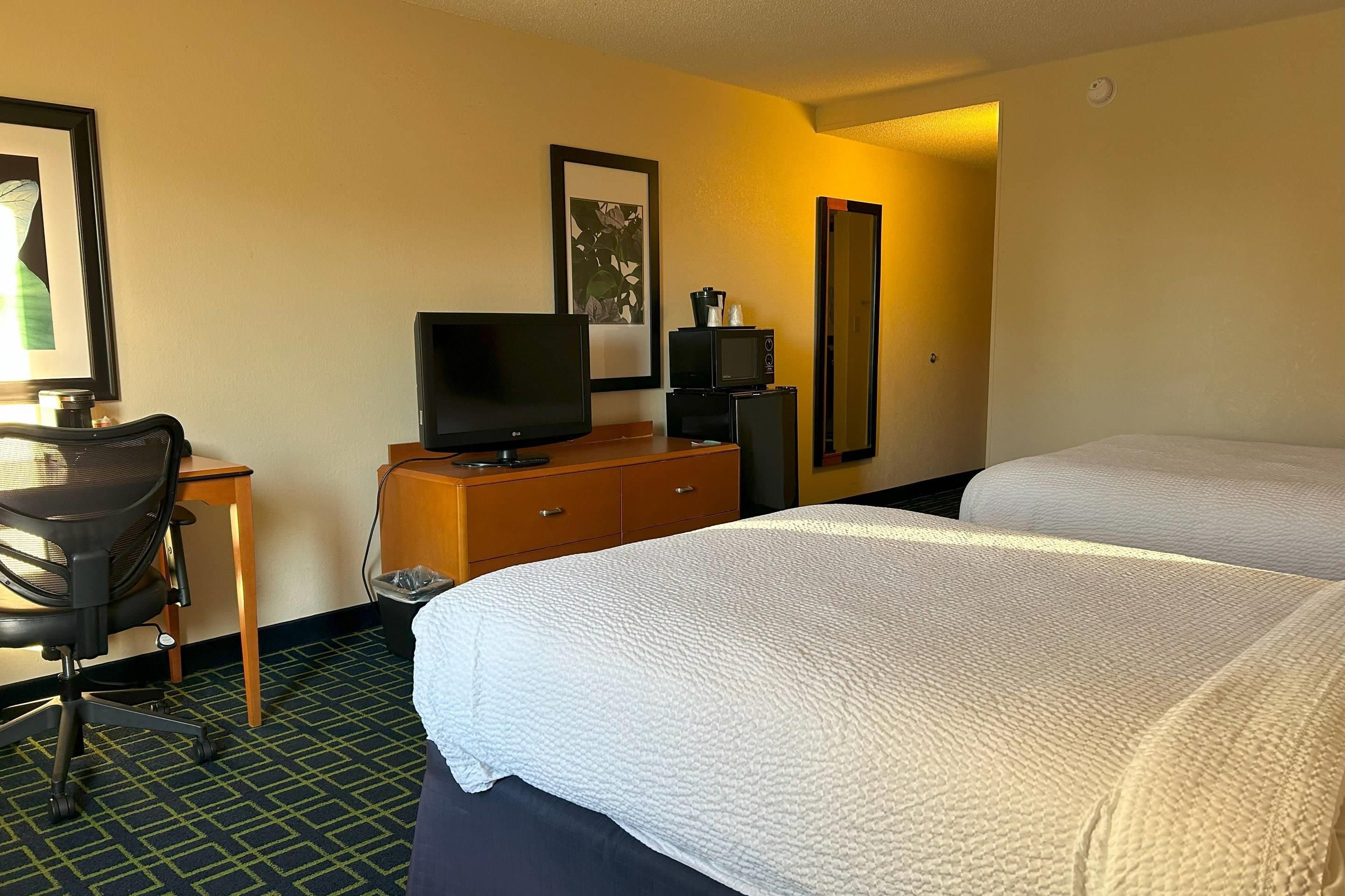 A hotel room with two beds, a desk with a television, a chair, a dresser, and a framed picture on the wall.