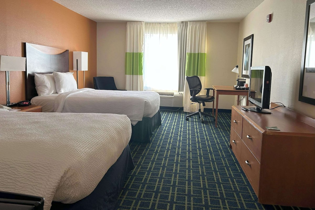 Habitación de hotel con dos camas, un escritorio con silla, cómoda, televisor y ventana con cortinas.