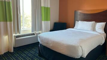A hotel room with a bed, a chair, a window with curtains, and a wall-mounted heater.