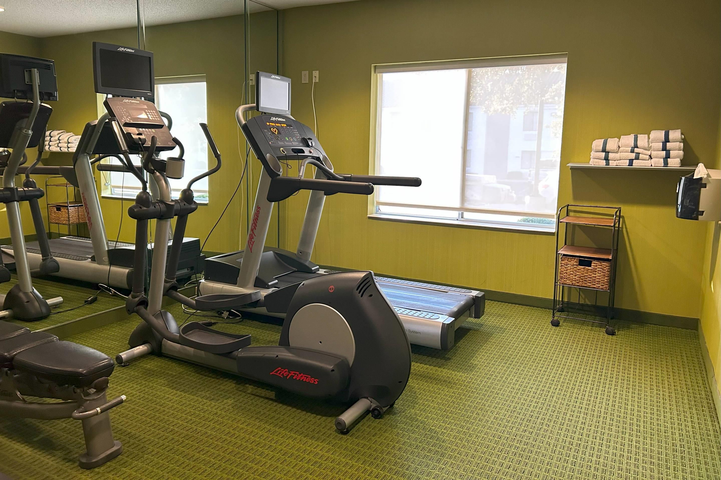Et fitnessrum med løbebånd, crosstrainere og en motionscykel.
