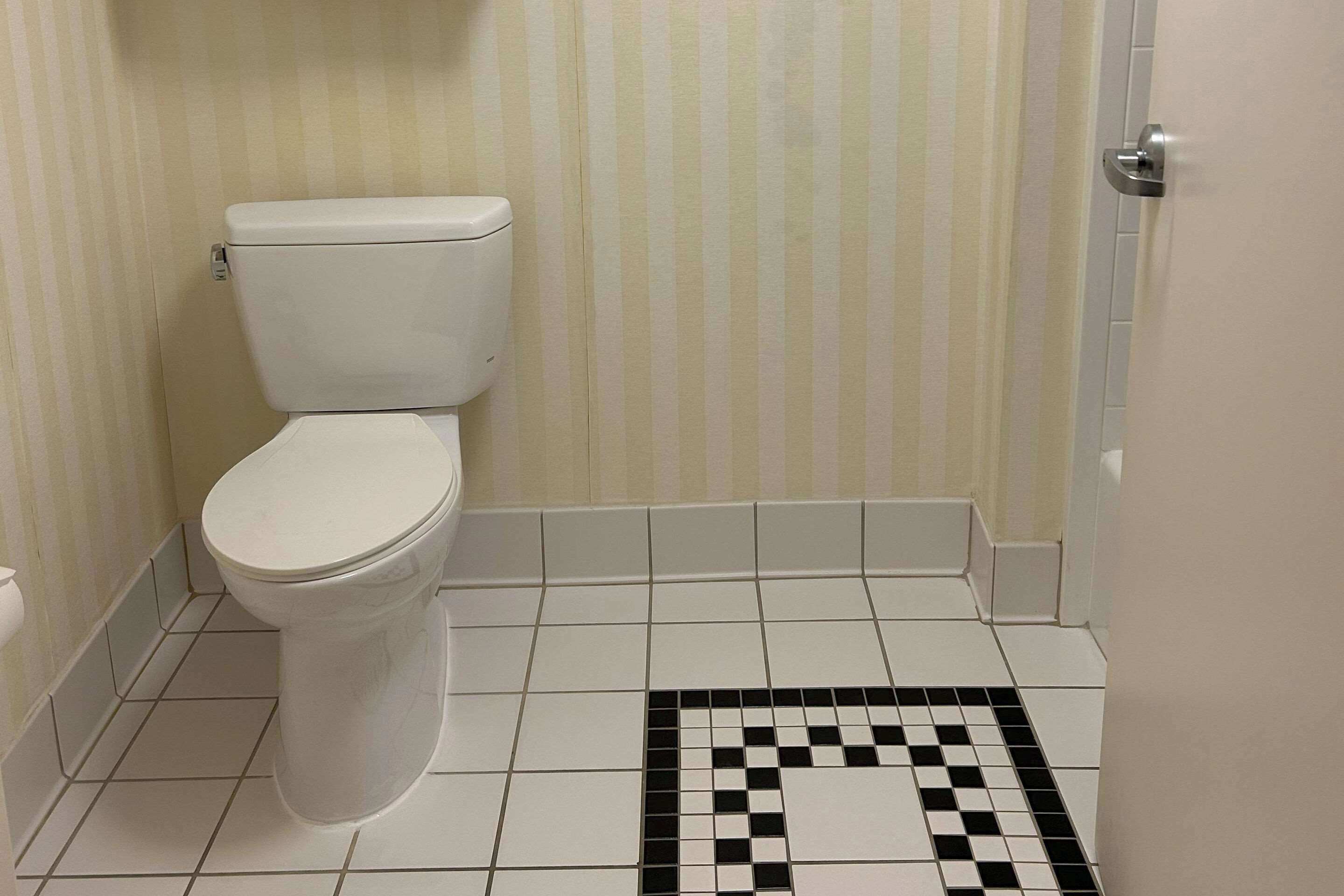 A bathroom with a toilet, striped wallpaper, and a black and white checkered floor pattern.