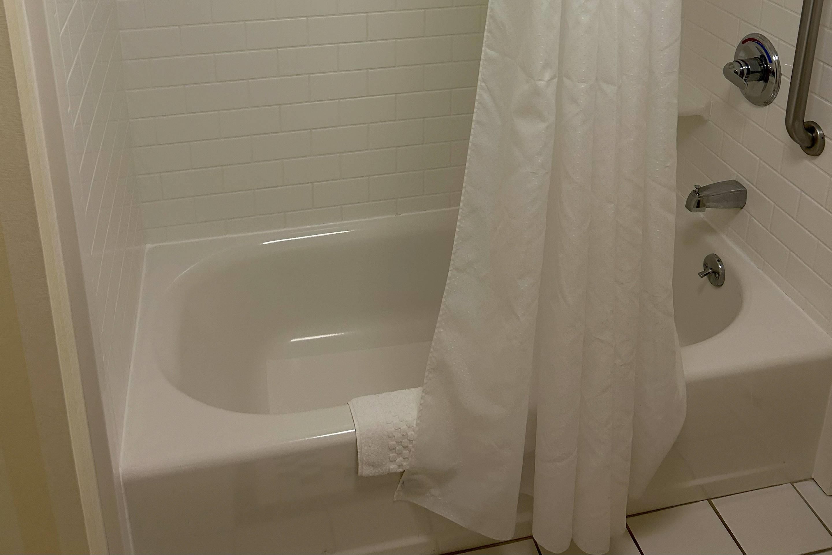 Una bañera blanca con cortina de ducha, una toalla y un grifo.