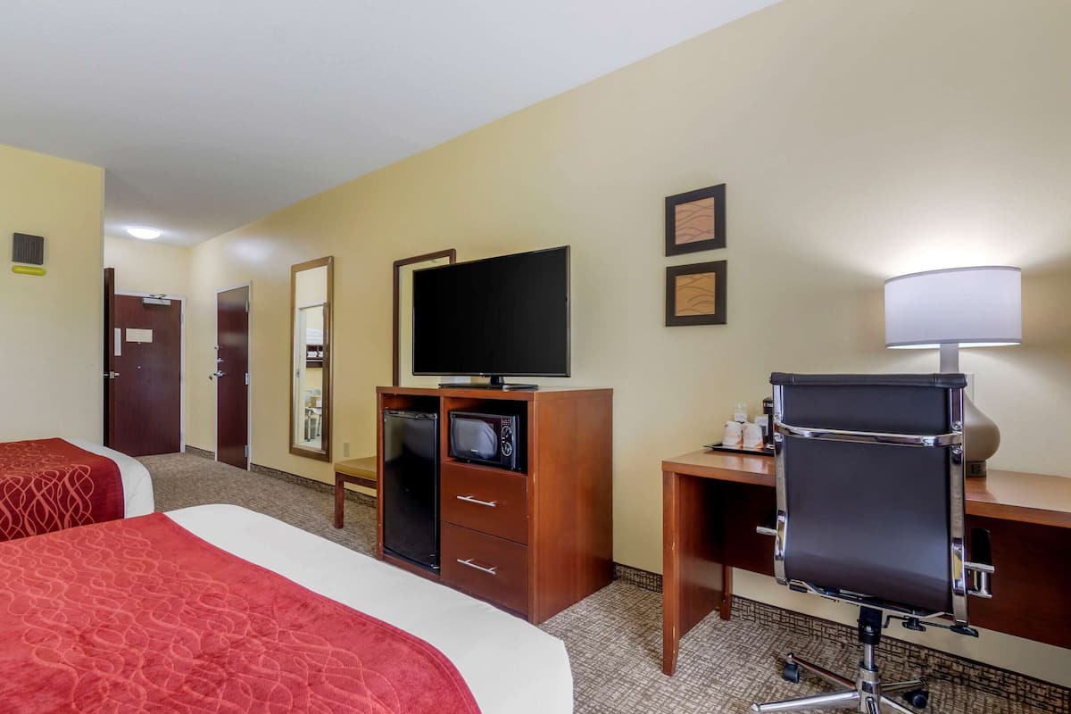 Une chambre d’hôtel avec deux lits, un bureau avec un ordinateur, une télévision et une lampe de bureau.