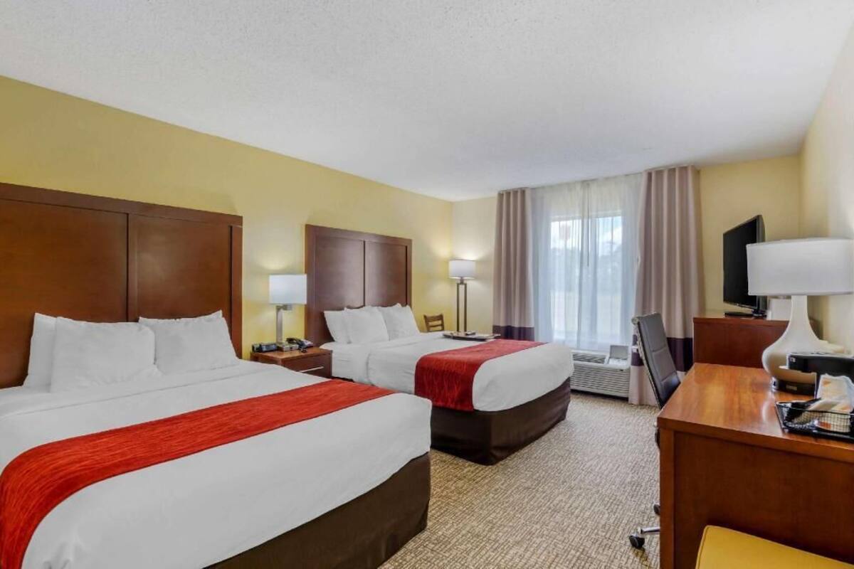 Une chambre d’hôtel avec deux lits, un bureau, une chaise, une télévision et une fenêtre avec des rideaux.