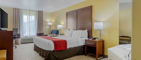 A hotel room with a bed, bedside tables, a desk, a chair, a TV, and a bathroom with a bathtub and sink.