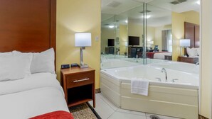 A hotel room with a bed, a bedside table with a lamp, a large mirror, and a bathtub.