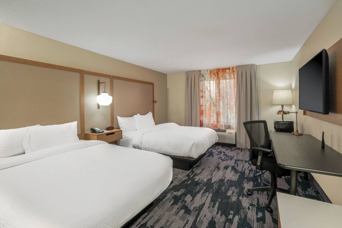 A hotel room with two beds, a desk, a chair, a TV, and a window with curtains.