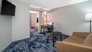 A hotel room with a flat-screen TV mounted on the wall, a desk with a chair, a sofa, and a lamp. - Fairfield Inn & Suites Memphis I-240 & Perkins (Memphis)