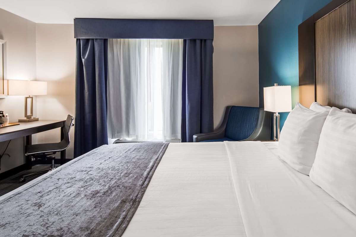 Una habitación de hotel con cama, escritorio, silla y ventana con cortinas.