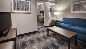 A hotel room with a blue sofa, a wooden coffee table, a patterned carpet, and framed artwork on the walls. - Best Western Town Center Inn (Weslaco)