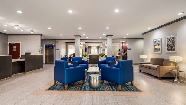 A modern lobby with a reception desk, blue seating area, and a kitchen in the background. - Best Western Town Center Inn (Weslaco)