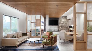 A modern living room with a wooden ceiling, large windows, a stone fireplace, and a dining area. - Fairfield Inn by Marriott Raleigh Airport/RTP (Morrisville)