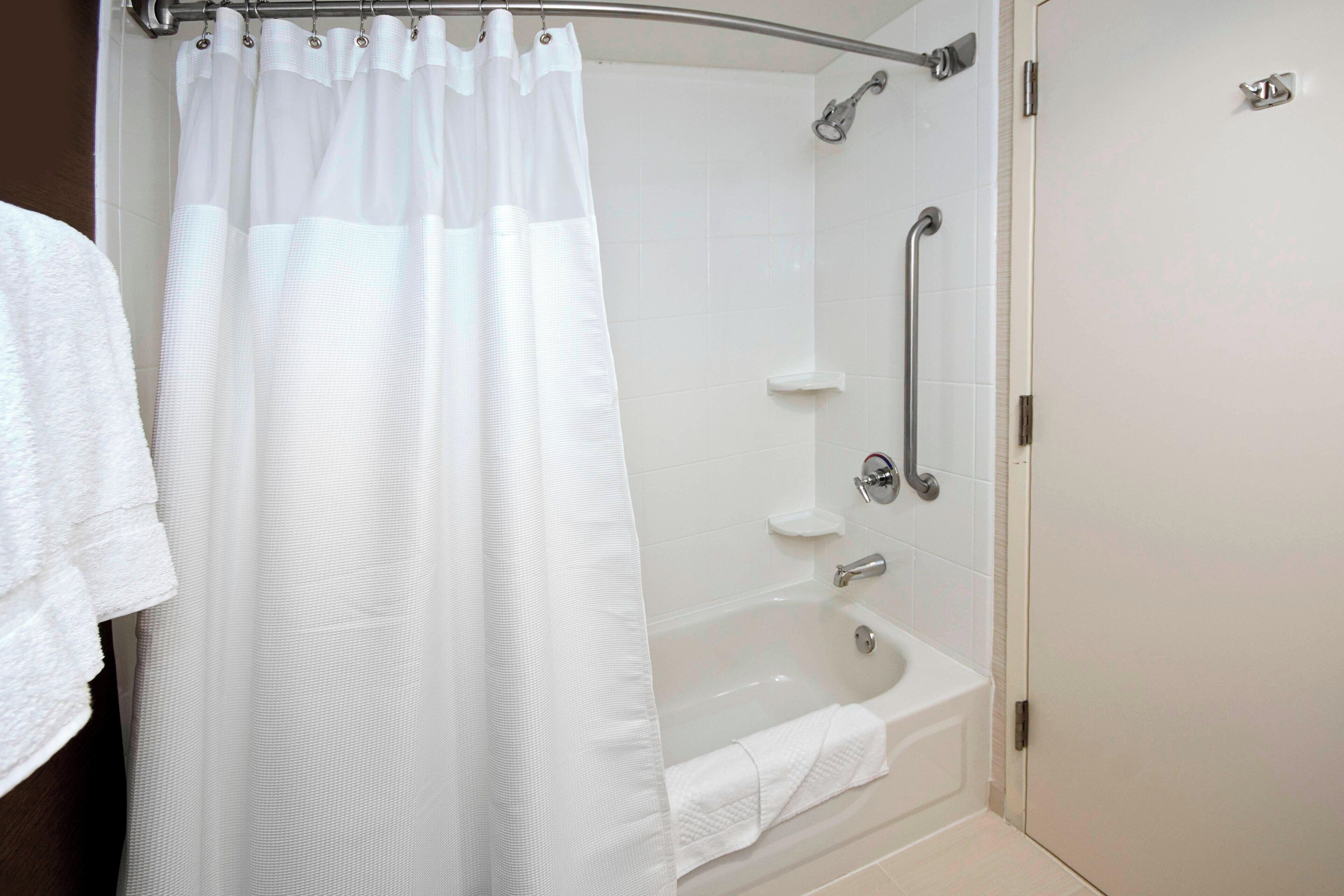 A modern bathroom with a glass shower enclosure, a bathtub, and a handrail.
