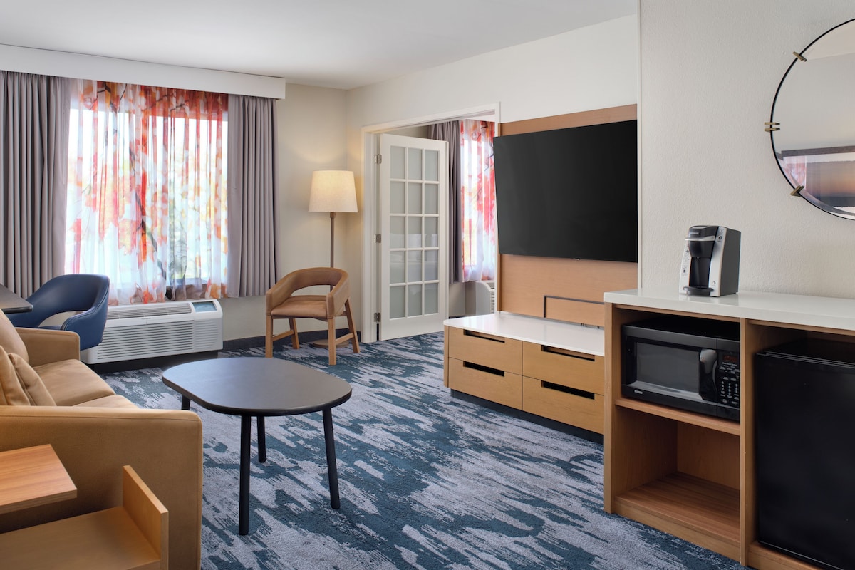 Une chambre d’hôtel équipée d’un canapé, d’un fauteuil, d’une petite table, d’une télévision, d’une machine à café et d’un four à micro-ondes.
