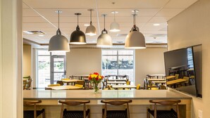 A modern interior with a central island, bar stools, hanging pendant lights, and a large flat-screen TV. - Fairfield Inn by Marriott Raleigh Airport/RTP (Morrisville)