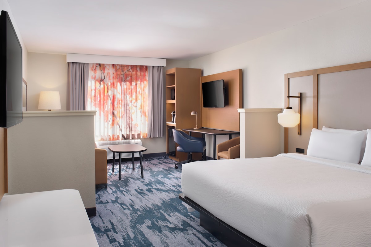 Une chambre d’hôtel avec un lit, un bureau, une chaise, une télévision et une fenêtre avec des rideaux.
