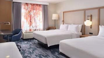 A hotel room with two beds, a desk, a chair, a lamp, and a large window with curtains.