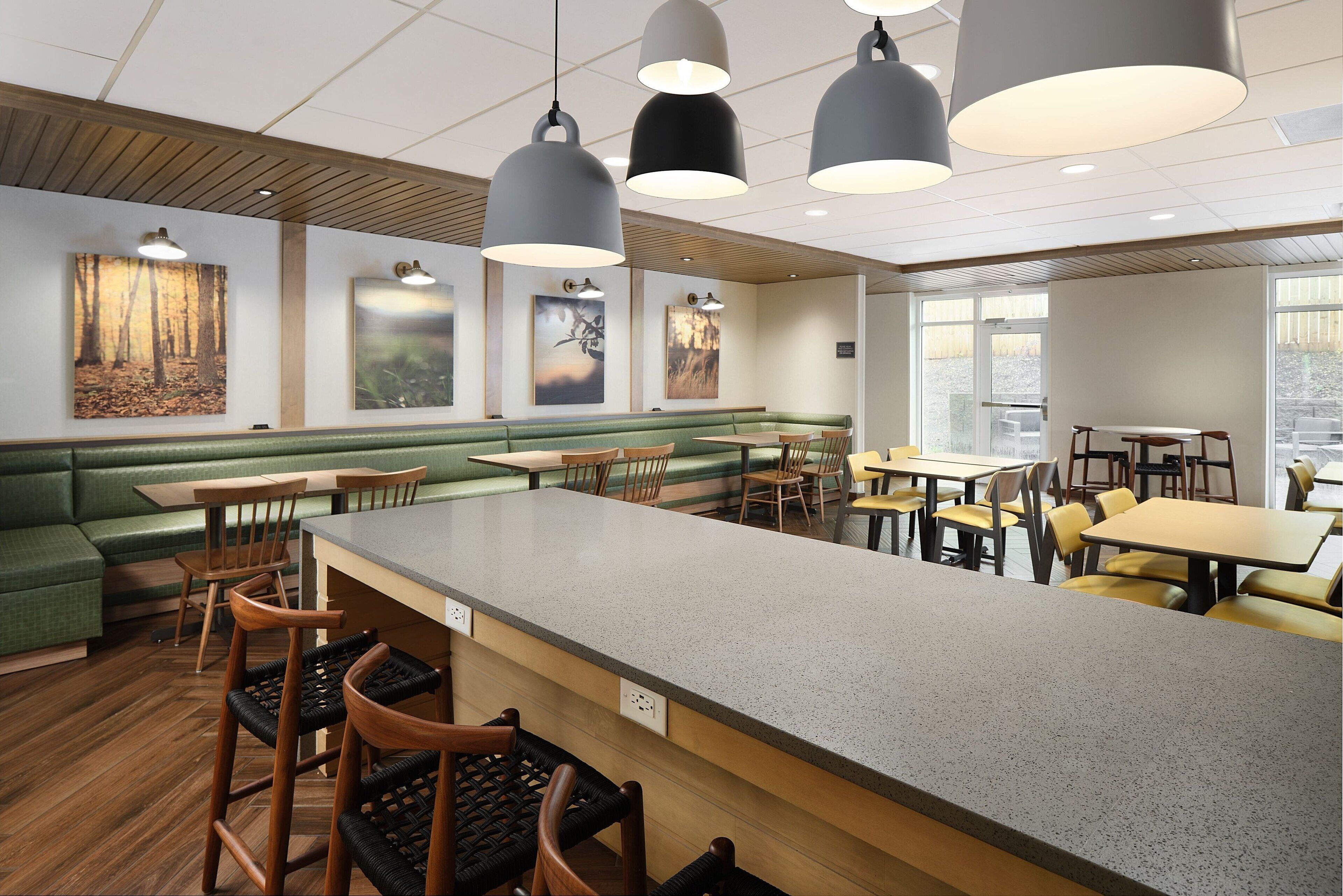 A modern restaurant with a central bar area, green seating, and artwork on the walls.