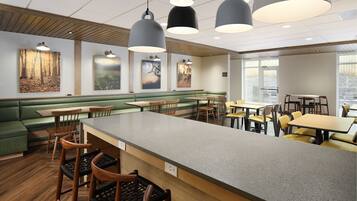 A modern restaurant with a central bar area, green seating, and artwork on the walls.
