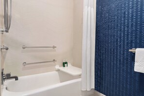 Un baño con una bañera blanca, zona de ducha y pared con estampado azul.