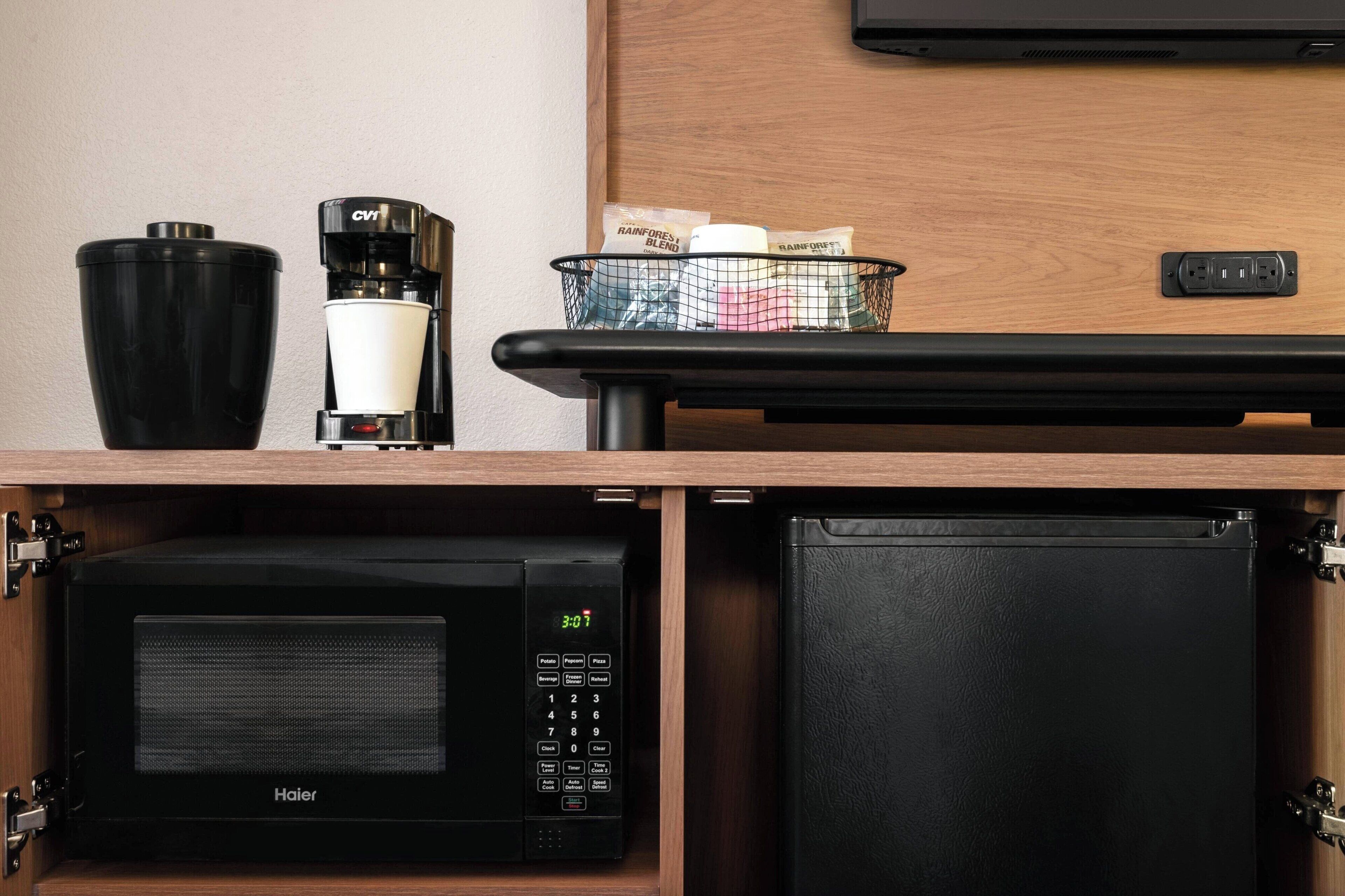 A compact kitchen area with a Haier microwave, a coffee maker, and a basket containing items on a wooden countertop.