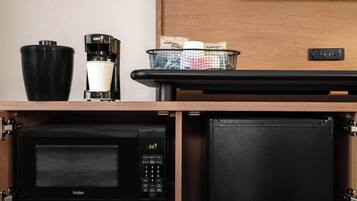 A compact kitchen area with a Haier microwave, a coffee maker, and a basket containing items on a wooden countertop.
