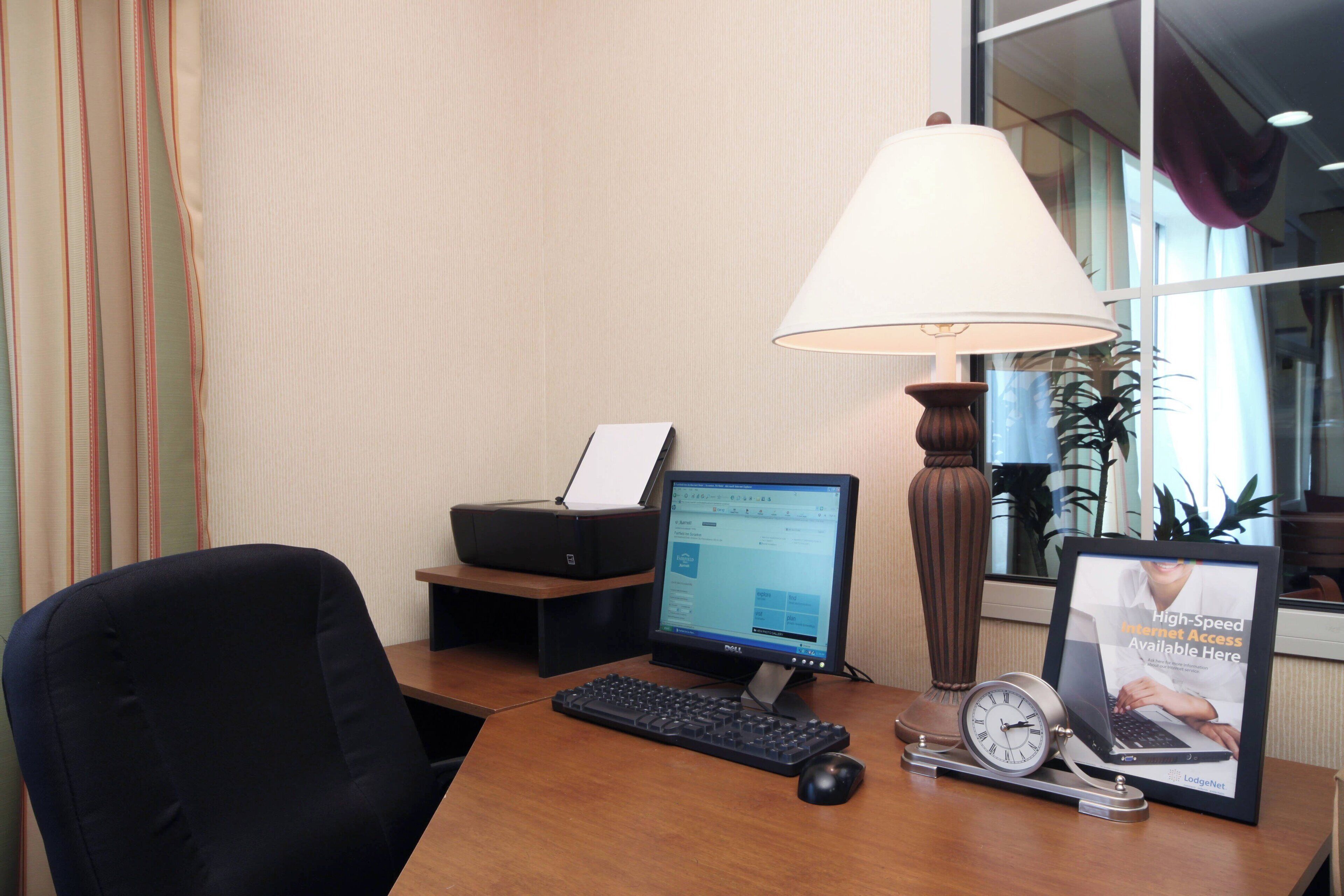 Un bureau avec un ordinateur, un clavier, une souris, une lampe, une horloge et un tableau encadré.