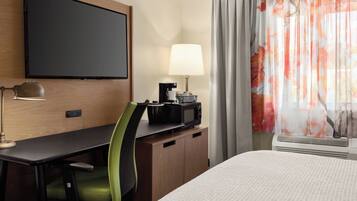 A hotel room with a bed, a desk with a chair, a television, a lamp, a coffee maker, and a window with curtains.