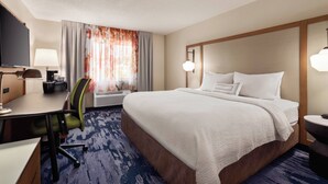 A hotel room with a large bed, a desk with a chair, a TV, and a lamp.