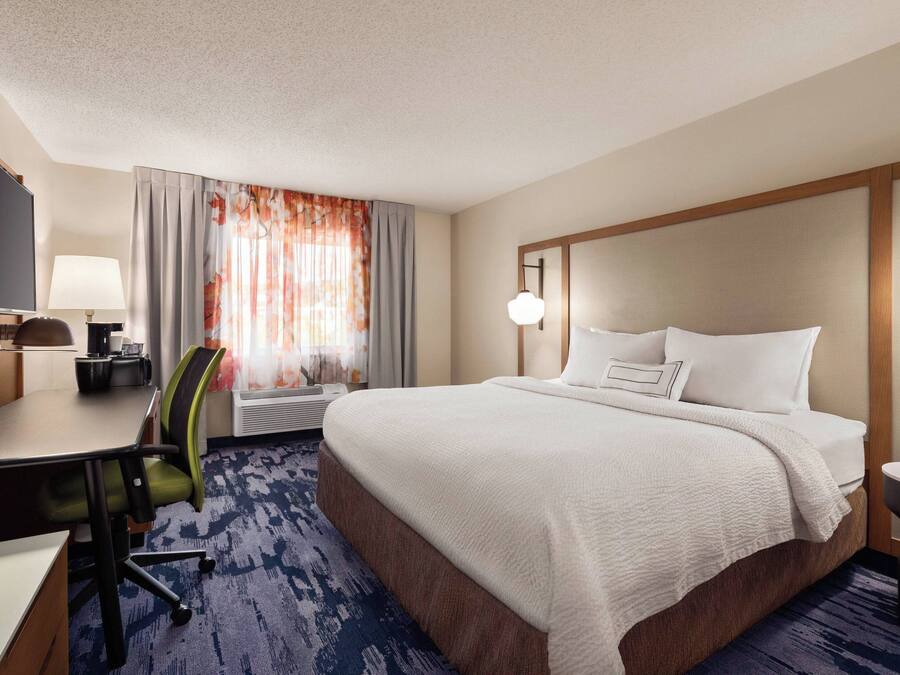 A hotel room with a large bed, a desk with a chair, a TV, and a lamp.