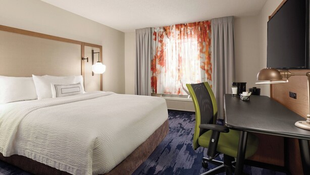 A hotel room with a bed, a desk, a chair, a television, and a window with curtains.