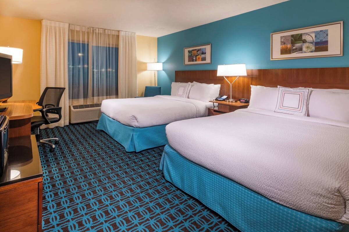 Ein Hotelzimmer mit zwei Betten, einem Schreibtisch mit Computer, einem Stuhl und einem Fernseher.