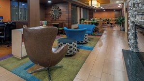 En hotellobby med en receptionsdisk, en sittgrupp med stolar och sittpuffar, en matplats och en vägg som är accentuerad med sten.