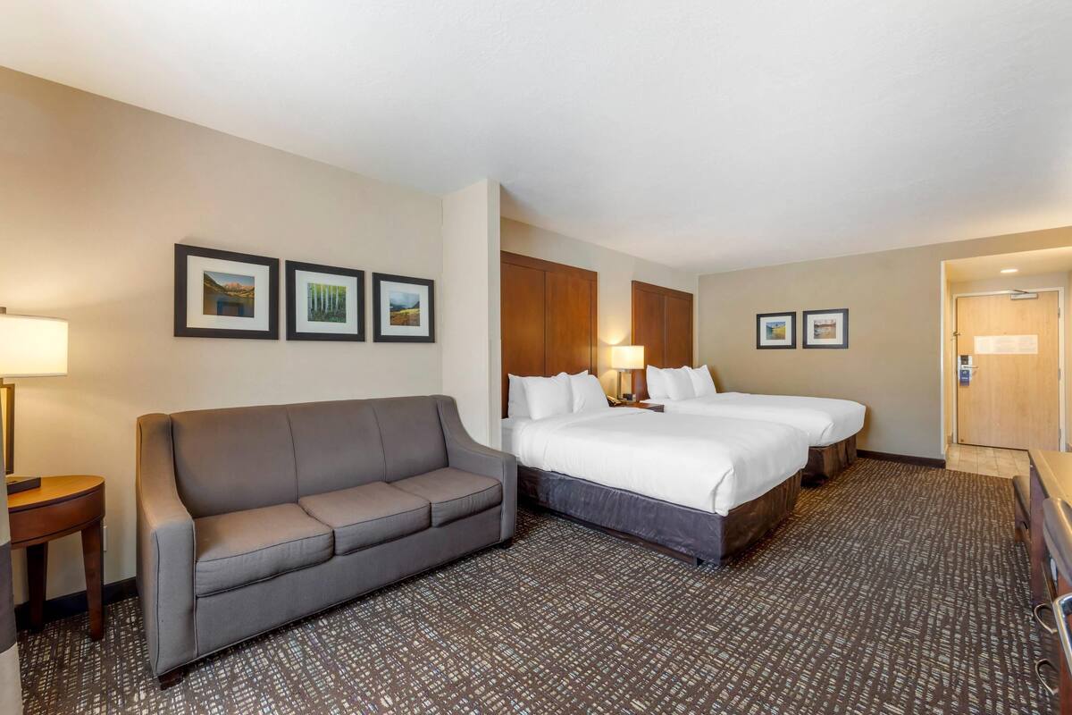 A hotel room with a bed, a sofa, and a desk. There are framed pictures on the wall.