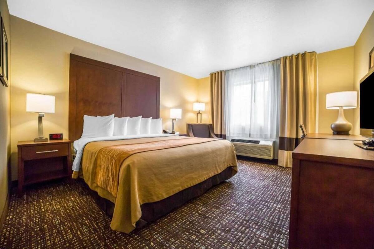 A hotel room with a bed, bedside tables, lamps, a desk, and a window with curtains.