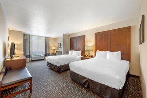Habitación de hotel con dos camas, un escritorio, una silla, un televisor y una ventana con cortinas.