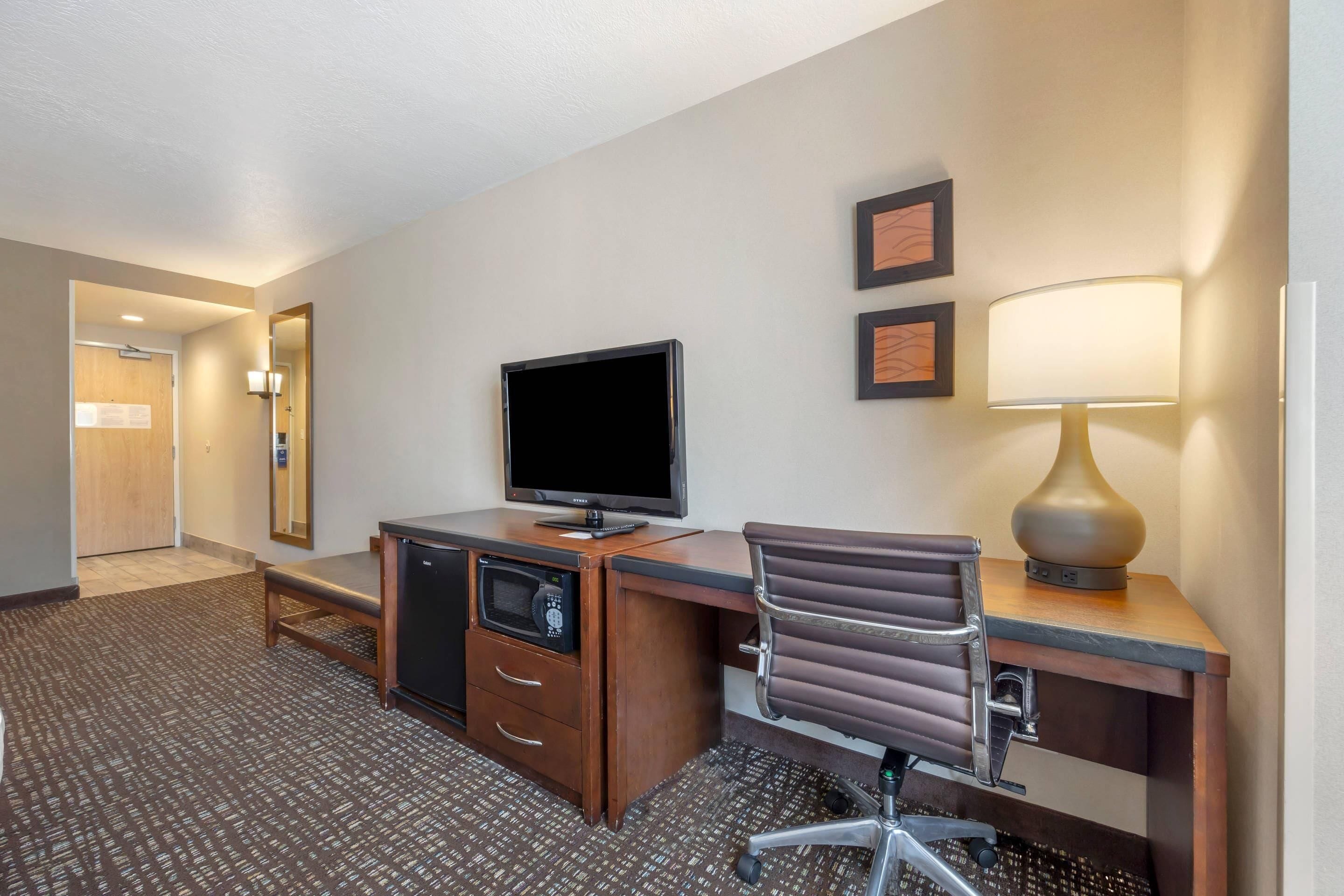 A hotel room with a desk, television, lamp, and microwave.