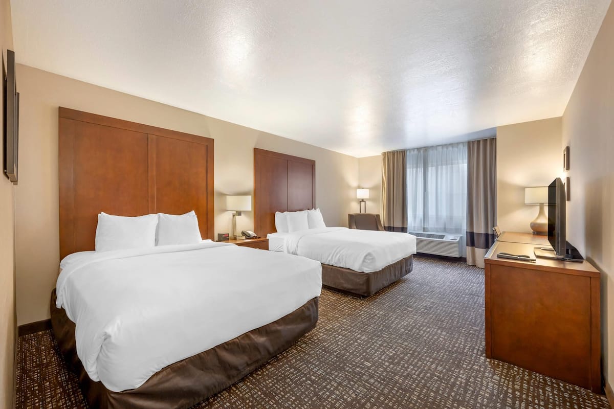 A hotel room with two beds, a desk, a TV, and a window with curtains.