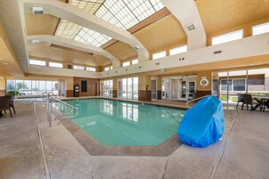 Piscina interior con techos de vidrio transparente, zona de estar cubierta y vistas al exterior.