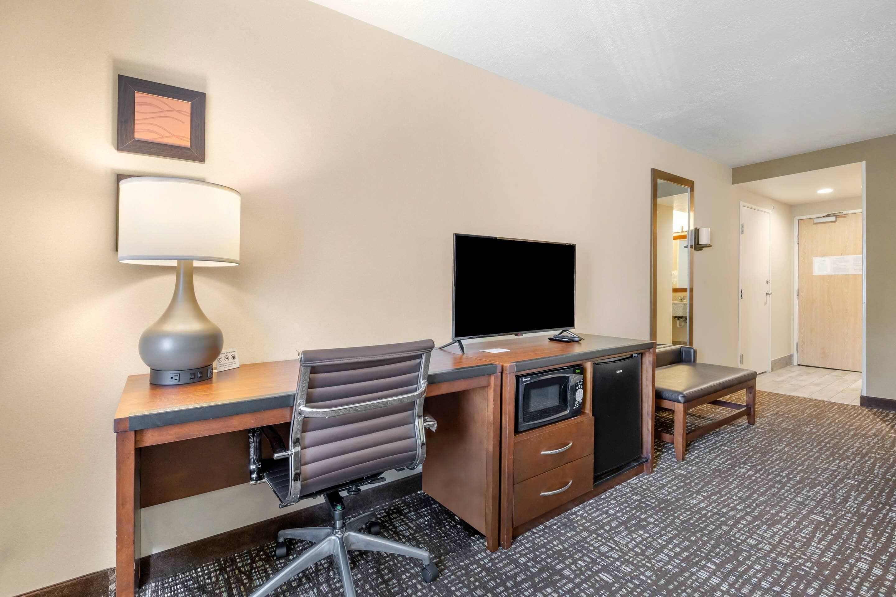 A hotel room with a desk, chair, television, microwave, and a small cabinet.