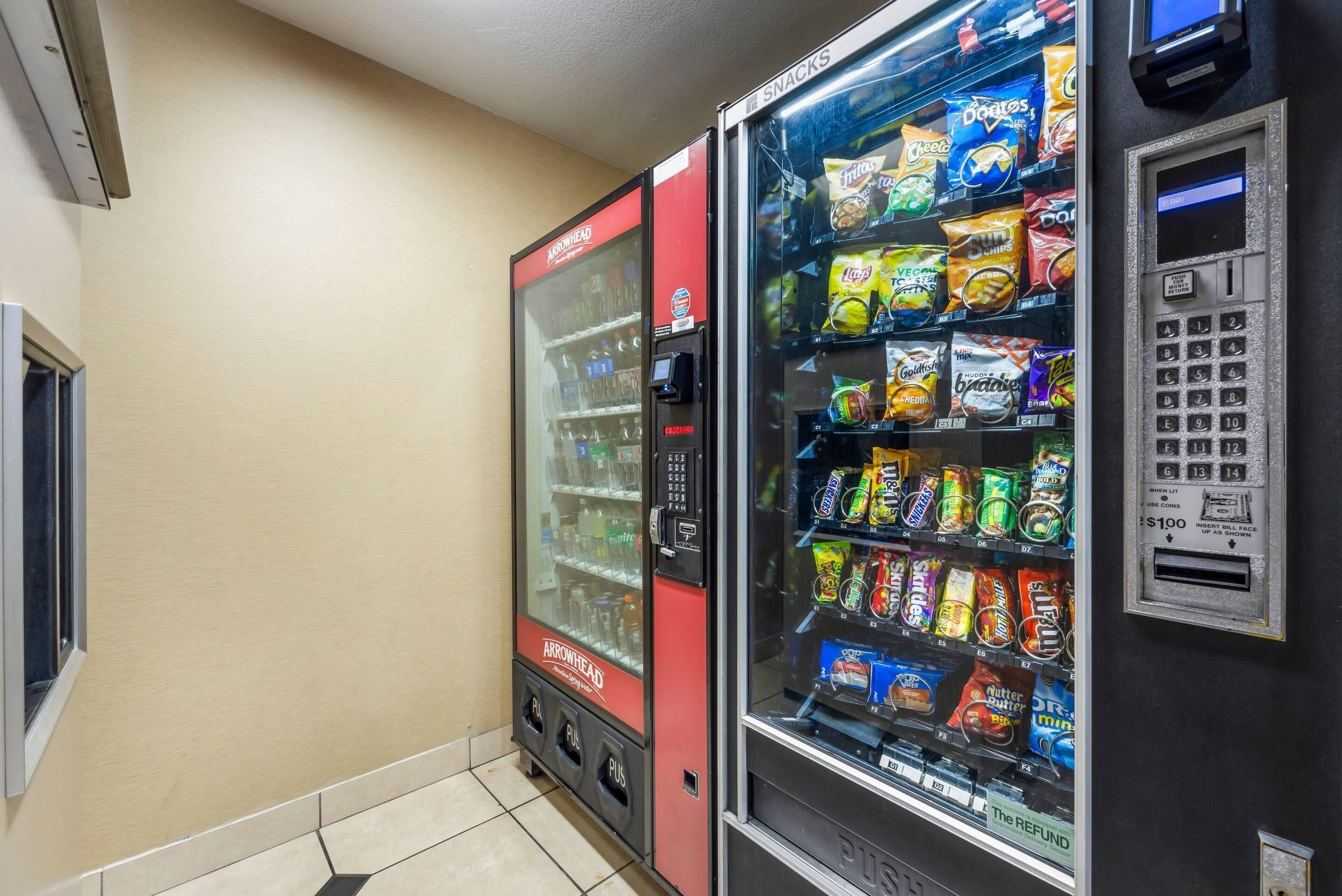 Máquina expendedora con aperitivos y bebidas, un terminal de pago y un respiradero en la pared.